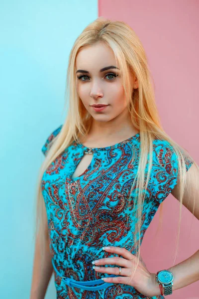 Hermosa mujer joven con reloj en un vestido azul con un patrón cerca de una pared de color azul brillante y rosa — Foto de Stock