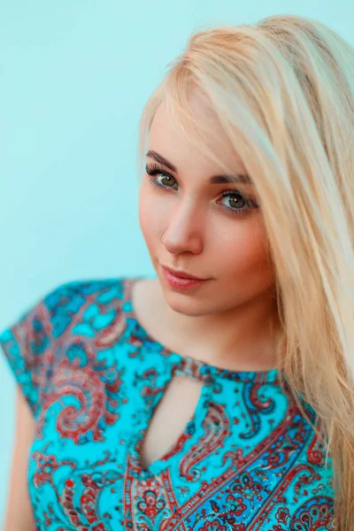 Retrato de uma bela jovem loira em vestido azul com padrões perto de uma parede azul brilhante — Fotografia de Stock