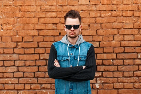 Portrait of a beautiful hipster man in a denim waistcoat near a brick wall — Stock Photo, Image