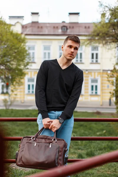 Красивий молодий чоловік у чорній футболці зі шкіряною сумкою, на відкритому повітрі — стокове фото