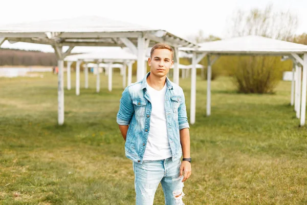 Şık genç adam Kot ceket ve kot bir beyaz T-shirt doğada dinleniyor