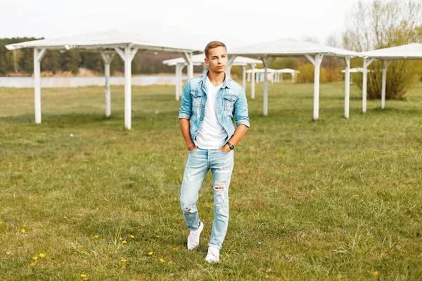 Yakışıklı adam şık denim giyim ve Beyaz tişört, beyaz saçak ile Sahilde yürüyüş spor ayakkabı