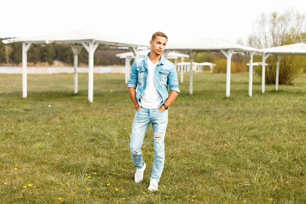 Yakışıklı genç bir kot ceket ve yırtık kot doğada yürüyüş ile beyaz T-shirt