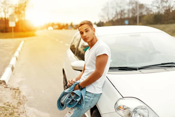 Un hombre guapo con una camiseta blanca cerca de un coche blanco. Viaje en coche — Foto de Stock