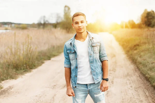 Yakışıklı genç bir kot ceket ve beyaz bir T-shirt batımında doğada yırtık kot pantolon ile
