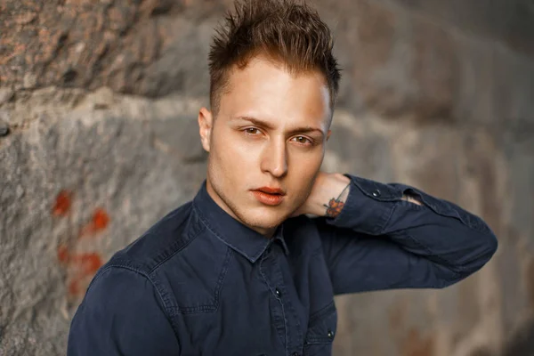 Retrato de cerca de un joven guapo con una camisa azul cerca de una pared de piedra — Foto de Stock