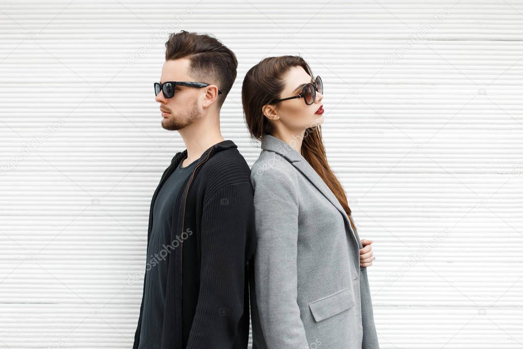 Beautiful young couple in sunglasses and stylish modern clothes near a wooden wall