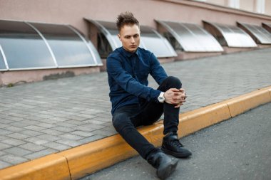 Siyah spor ayakkabı, kot kaldırım kenarında oturan mavi tişört ile genç adam