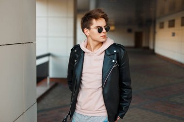 genç yakışıklı bir siyah deri ceket ve modern beyaz bir duvar yakınındaki pembe bir kazak havacı güneş gözlüğü