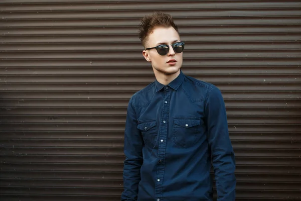 Joven guapo de moda en gafas de sol posando cerca de la pared de metal — Foto de Stock