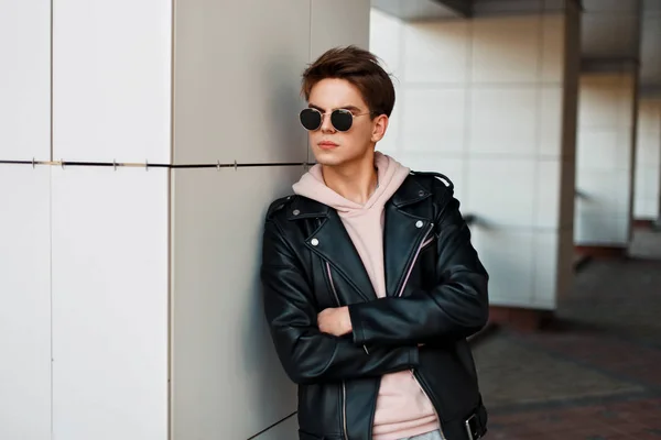 ファッショナブルなブランドのサングラスでハンサムな若い男のジャケットが白い壁の近くに立って — ストック写真