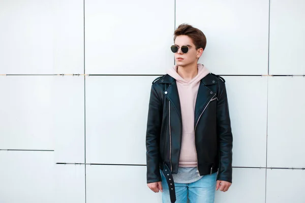 Beau jeune homme en lunettes de soleil et vêtements à la mode près d'un mur blanc — Photo