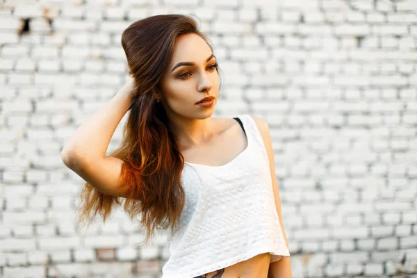 Schöne junge Frau in einem weißen stylischen T-Shirt posiert in der Nähe einer weißen Mauer aus Ziegelsteinen — Stockfoto