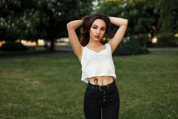Piękna młoda kobieta w białe koszulki i czarne dżinsy pozowanie w parku w letni dzień — Zdjęcie stockowe