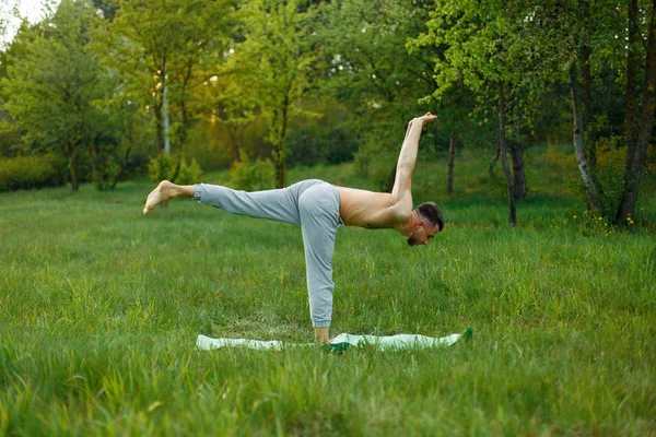 Junger Mann praktiziert Yoga im Garten auf dem grünen Gras — Stockfoto