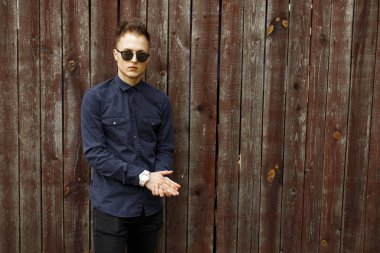 Adam mavi gömlek ve siyah pantolon yakınındaki bir ahşap duvar ile moda güneş gözlüğü