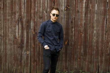 Yakışıklı delikanlı şık giysiler ve bir ahşap duvar yakınındaki güneş gözlüğü