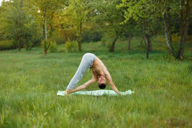 Genç adam parkta yoga yapıyor.