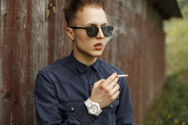 Elegante hombre guapo fumando un cigarrillo cerca de una pared vintage — Foto de Stock