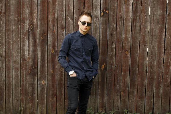 Yakışıklı delikanlı şık giysiler ve bir ahşap duvar yakınındaki güneş gözlüğü