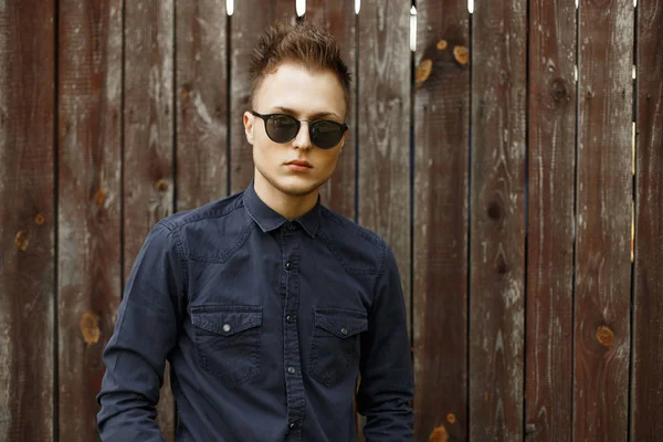 Vintage Porträt eines jungen Mannes mit Sonnenbrille und blauem Hemd in der Nähe einer alten Holzwand — Stockfoto