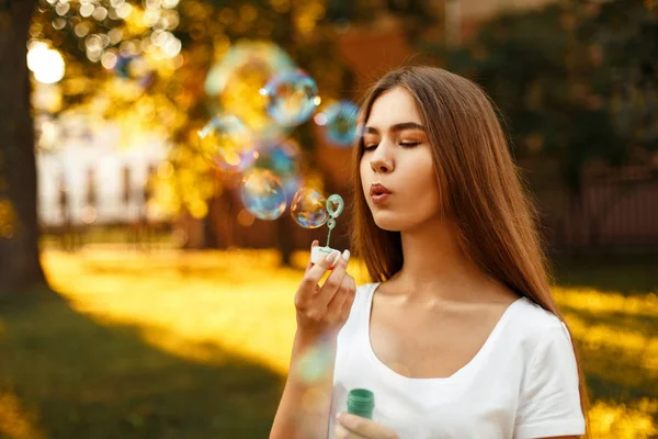Hermosa joven que sopla burbujas de jabón en el parque en un día de verano al atardecer — Foto de Stock