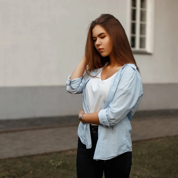 Joven chica con estilo en una camisa azul y una camiseta blanca posando cerca de la pared de la casa —  Fotos de Stock