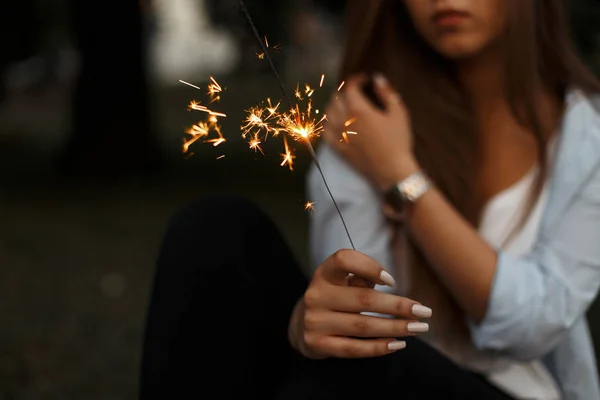 Mujer sostiene un fuego chispeante con una chispa en la noche de verano — Foto de Stock