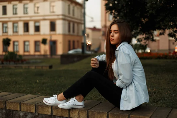 Genç güzel kadın parkta bir maytap geri kalanı ile mavi bir gömlek ve beyaz spor ayakkabı