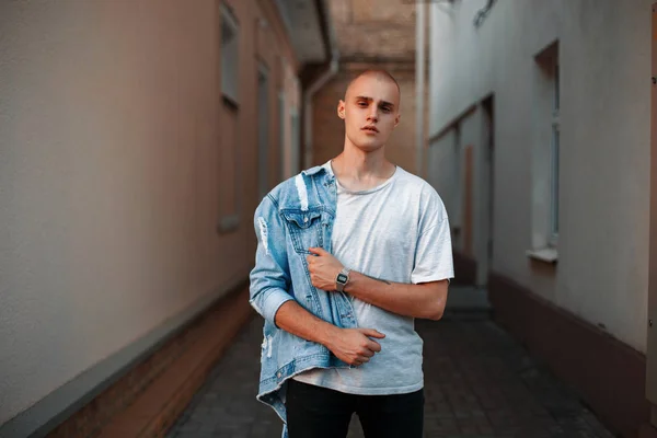 Joven americano guapo de moda en una chaqueta de mezclilla y una camiseta gris en la calle — Foto de Stock