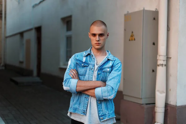 Elegante joven modelo hombre en una chaqueta jeans en una calle cerca de un edificio — Foto de Stock