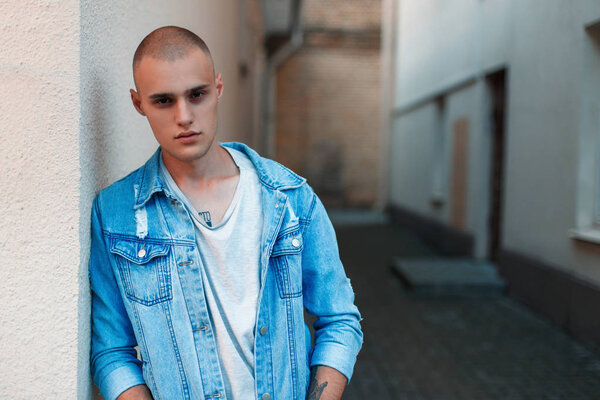 Handsome stylish American man in a denim jacket and a gray T-shirt near a building on the street