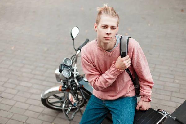Молодий хлопець в рожевому светрі і рюкзак сидить на мотоциклі — стокове фото