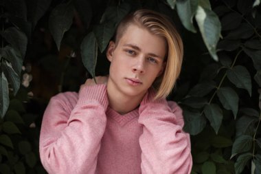 Şık yakışıklı genç pembe moda kazaklı bir yeşil yeşillik yakınındaki bir saç modeli ile