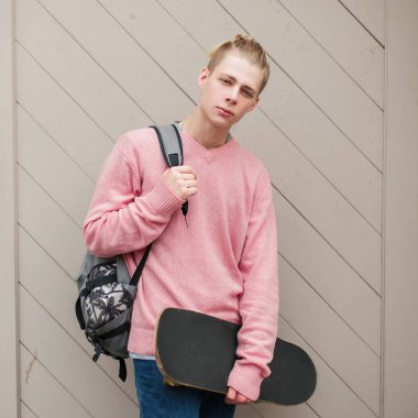 Yakışıklı genç model Pembe moda kazaklı bir sırt çantası ve kaykay ile bir saç modeli ile