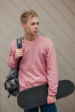 Bir sırt çantası ve plaja yakın bir ahşap duvar kaykay ile genç moda yakışıklı adam