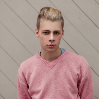 Yakışıklı genç bir pembe kazaklı bir ahşap duvar yakınındaki bir saç modeli ile