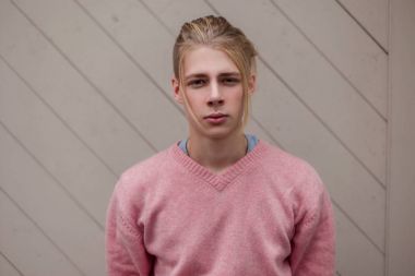 Yakışıklı genç erkek model Pembe moda kazaklı bir ahşap duvarının yakınında