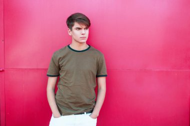 Şık genç adam bir T-shirt ve pembe bir metal duvar yakınındaki beyaz pantolon