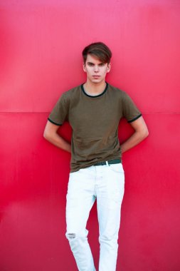 Klasik bir T-shirt ve pembe bir metal duvar yakınındaki beyaz pantolon yakışıklı genç