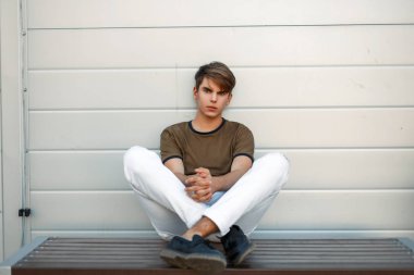 yakışıklı genç moda giysiler içinde bir metal duvar yakınındaki bir bankta oturuyor