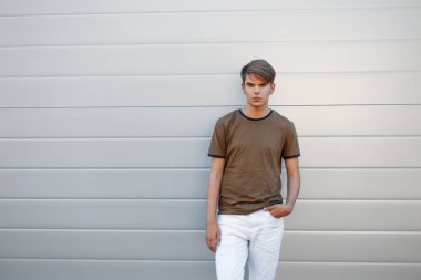 Şık yakışıklı bir T-shirt ve gri parlak duvarının yakınında beyaz pantolon