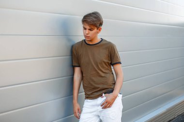 yakışıklı genç bir moda T-shirt bir saç modeli ile modern bir parlak duvara yakın duruyor