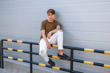 Şık yakışıklı delikanlı duvara yakın oturan trendy yaz giysileri