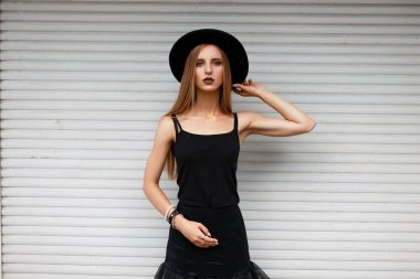 Beyaz duvar yakınındaki bir şapka ile siyah moda giysileri güzel şık kadın