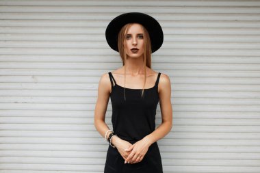 Beyaz duvar yakınındaki şapka ile siyah giysili güzel genç kadın