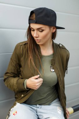 Güzel genç kadın modeli ile Çiller bir beyzbol şapkası ve gümüş duvarının yakınında şık yeşil bir askeri ceket