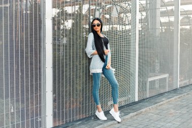 Uzun saç moda iyi giysiler ve duvarın yanında beyaz spor ayakkabı ile şık güzel model kız