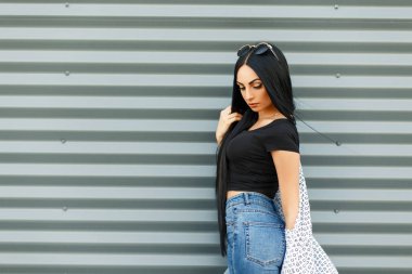 Siyah şık T-shirt ve kot yüksek bel metal bir duvara yakın poz ile güzel ve genç birbayan