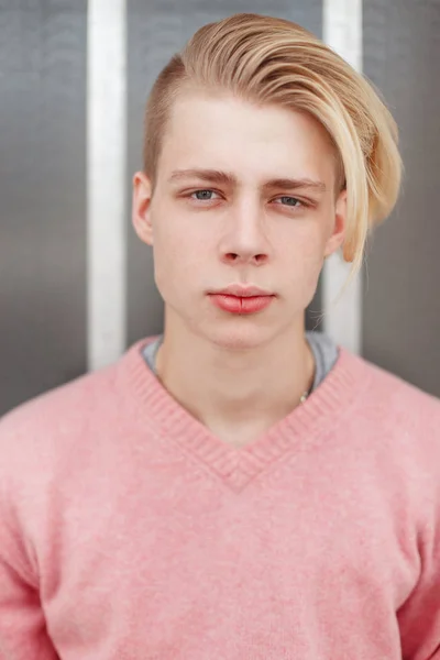 Portrait d'un beau jeune homme avec une coiffure blonde dans un pull rose près du mur — Photo